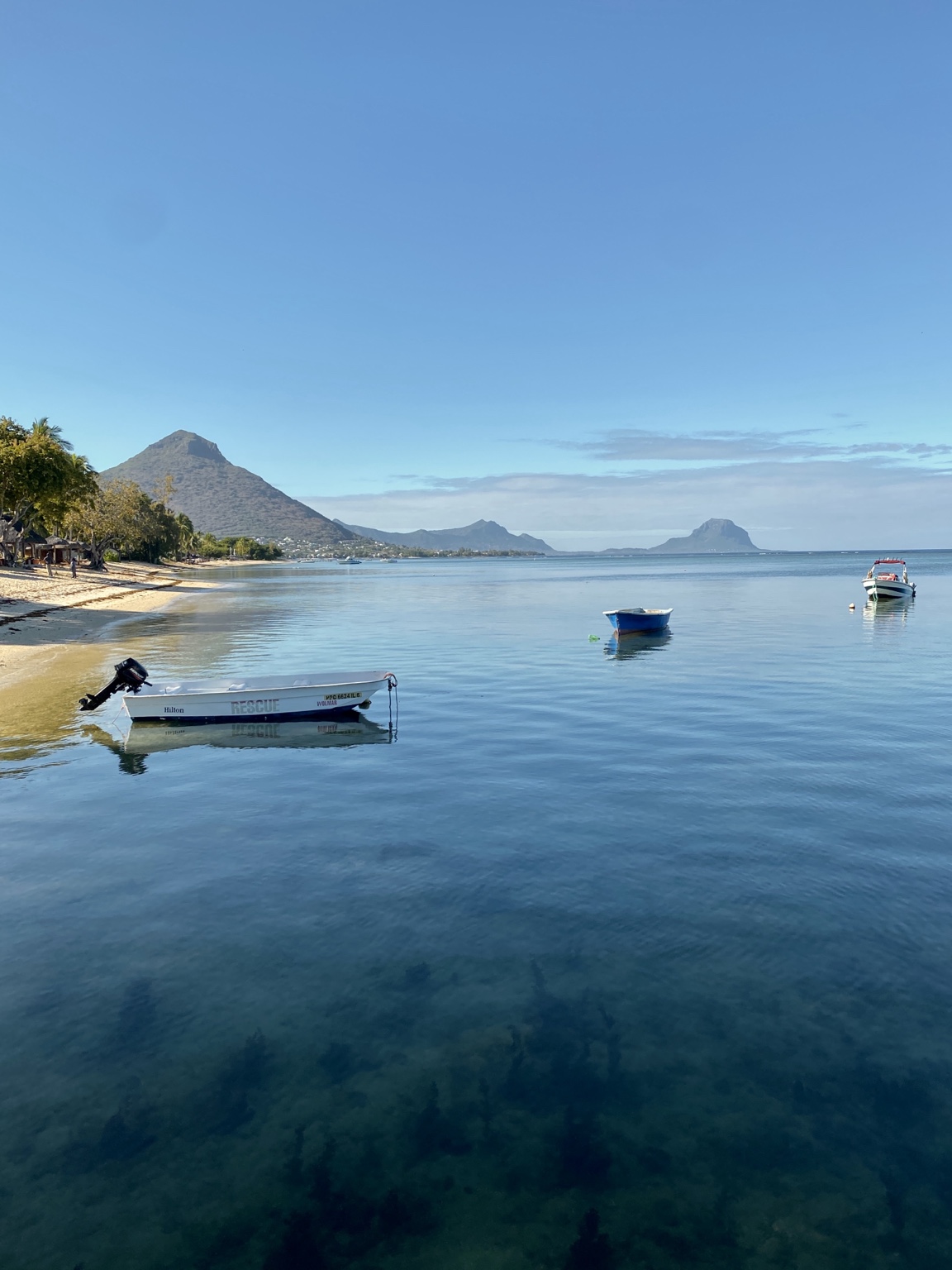 Boats resting in a calm blue bay beside a beach and the mountains of Mauritius