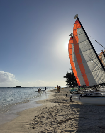 A sailboat with orange and white sails on a Mauritian beach